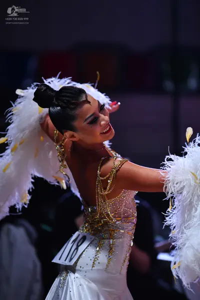 Dancesport competitor: Female dancer: white latin dress with gold sequin embellishments and large white