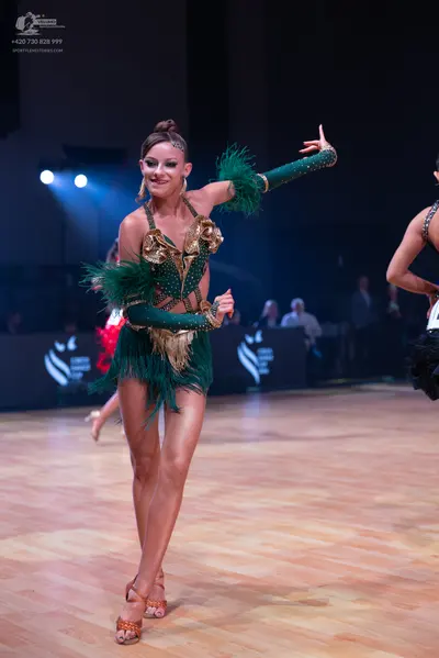 Dancesport competitor: Female dancer: emerald green Latin dress with gold sequin bodice and long green 