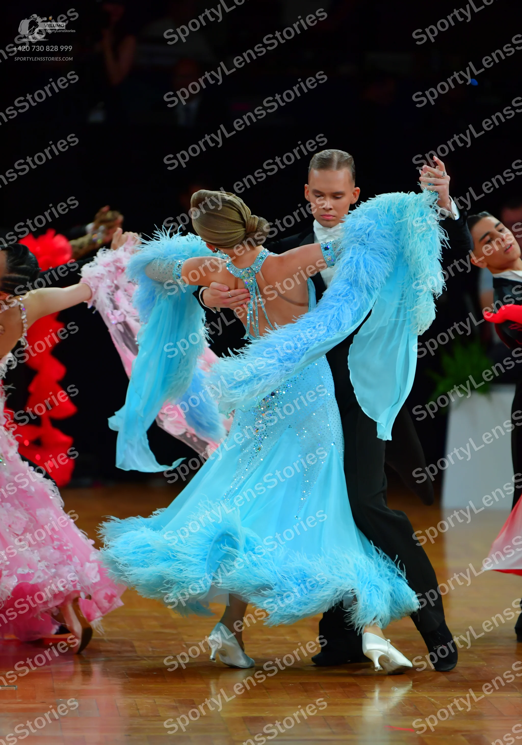 Dancesport competitor: Female dancer in center: light blue ballroom dress with feathery trim on the sle