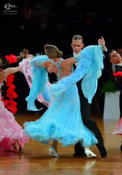 Dancesport competitor: Female dancer in center: light blue ballroom dress with feathery trim on the sle