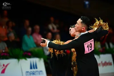 Dancesport competitor #19: Male dancer: black long-sleeved dance top with gold feathery accents on the shou