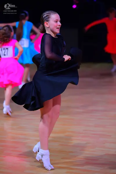 Dancesport competitor: Female dancer in foreground: black long-sleeved dress with a flowing skirt