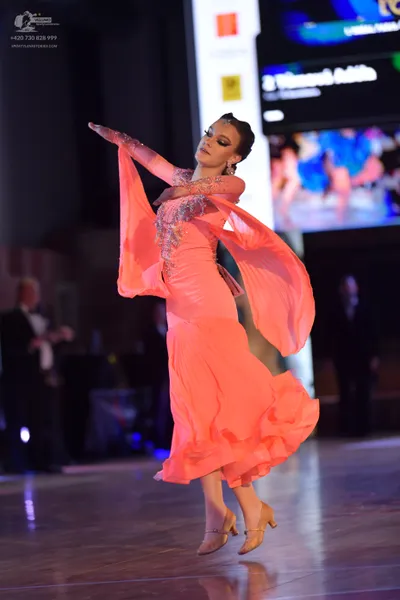 Dancesport competitor: Female dancer: peach-colored ballroom dress with wide, flowing sleeves, sparklin