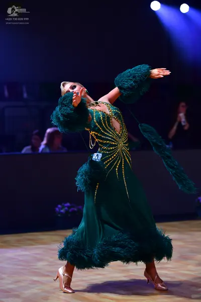 Dancesport competitor: Female dancer: emerald green ballgown with gold/yellow sequin/beadwork in a radi