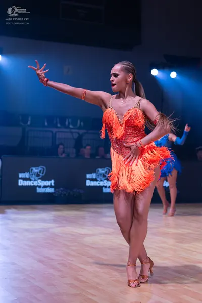Dancesport competitor: Female dancer in foreground: orange latin dress with fringe and sequins, and ora