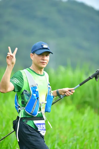 Marathon runner #389: Runner 1: green shirt, black shorts, blue and white hydration vest, blue cap, an