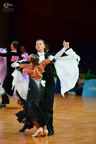 Dancesport competitor: Male dancer in foreground: black suit, white shirt, and white bow tie