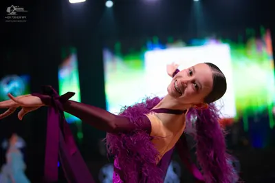 Dancesport competitor: Female dancer in foreground: purple Latin dance dress with feather detailing on 