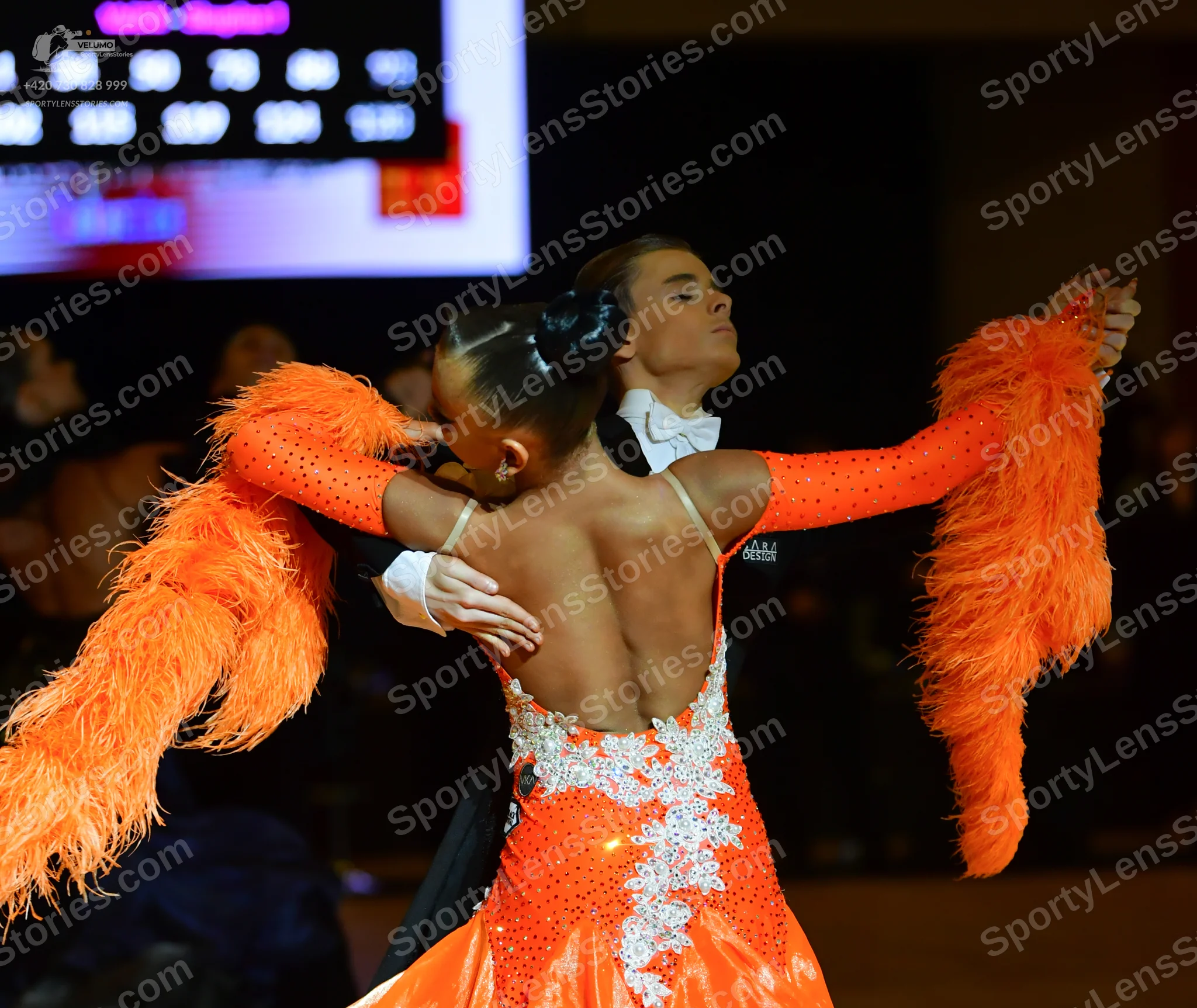 Dancesport competitor: Female dancer: orange Latin dance dress with large orange feather fringes on the