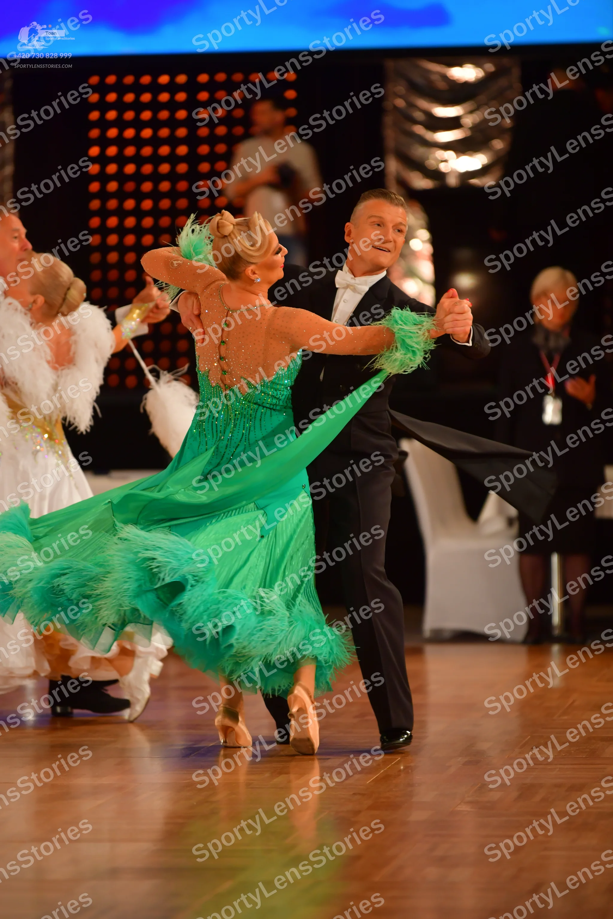 Dancesport competitor: Female dancer in foreground: green latin dress with sequins and fringe