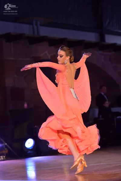 Dancesport competitor: Female dancer: peach-colored ballroom dress with long, flowing, split sleeves ma