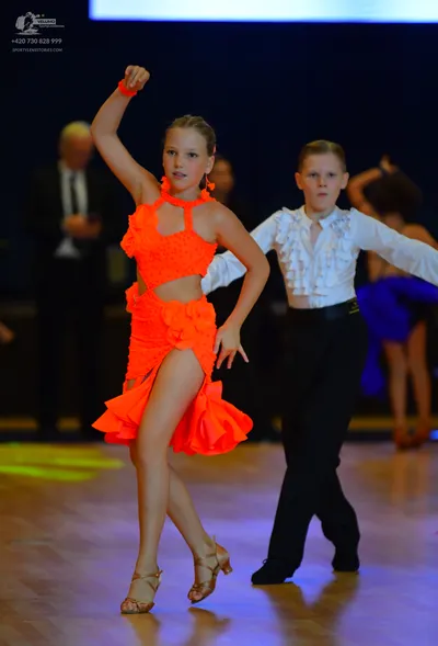 Dancesport competitor: Female dancer: bright orange ruffled Latin dance dress with a cutout waist and h
