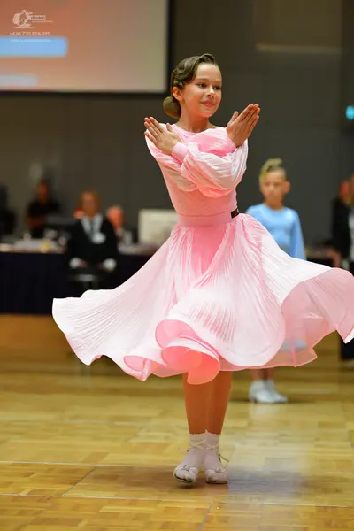 Dancesport competitor: Female dancer in foreground: light pink long-sleeved ballroom dress with a large