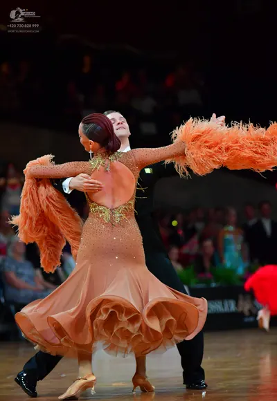Dancesport competitor: Female dancer: peach-colored long-sleeved dress with a ruffled skirt and large p