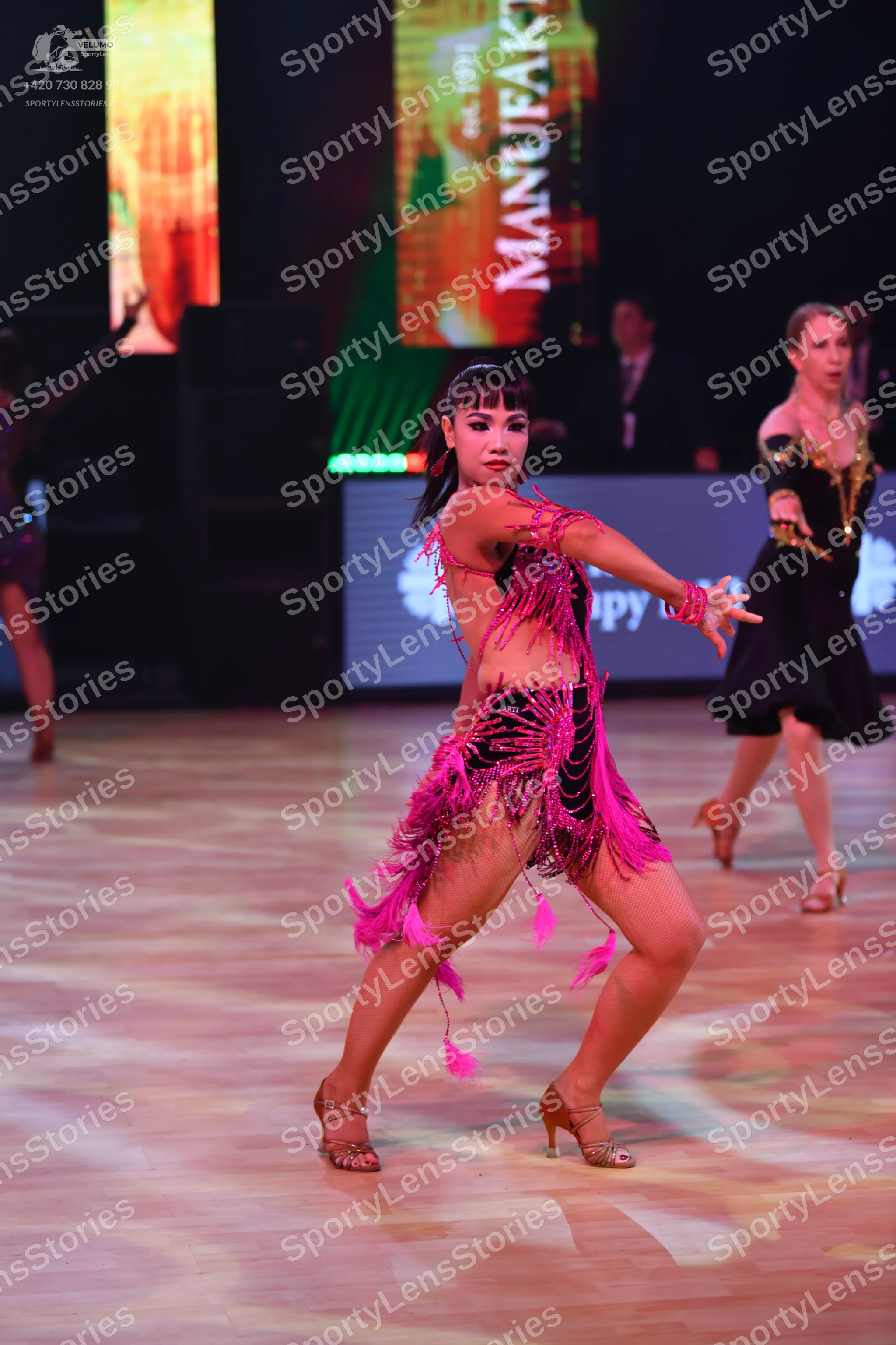 Dancesport competitor: Central female dancer: magenta pink Latin dance costume with long fringe and seq
