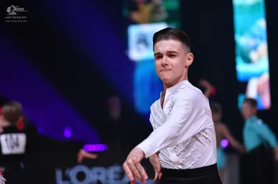 Dancesport competitor: Male dancer in foreground: white long-sleeved shirt with ruffles on the front an