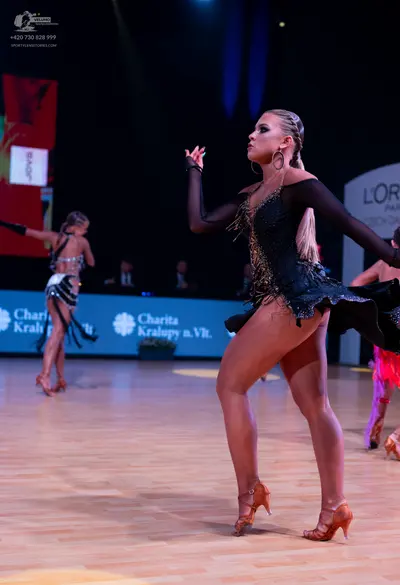 Dancesport competitor: Female dancer (foreground): black long-sleeved Latin dress with gold sequins and