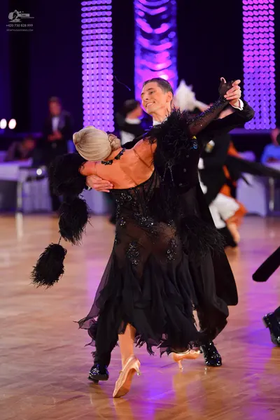 Dancesport competitor: Female dancer: black latin dress with a sheer, sequined bodice and large black f