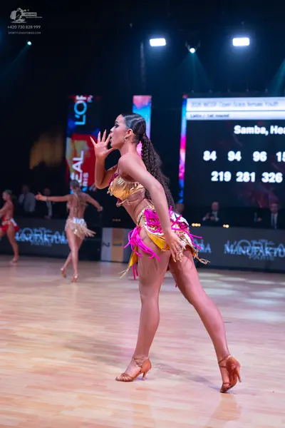 Dancesport competitor: Female dancer in foreground: gold sequined bra top and gold skirt with pink frin