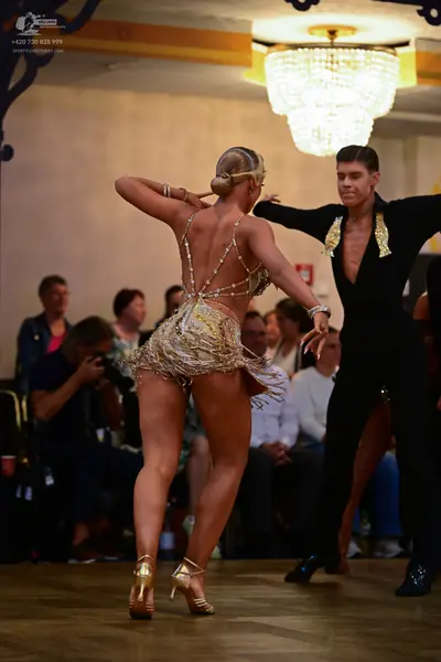 Dancesport competitor: Male dancer: black latin dance outfit with gold sequined embellishments on the c