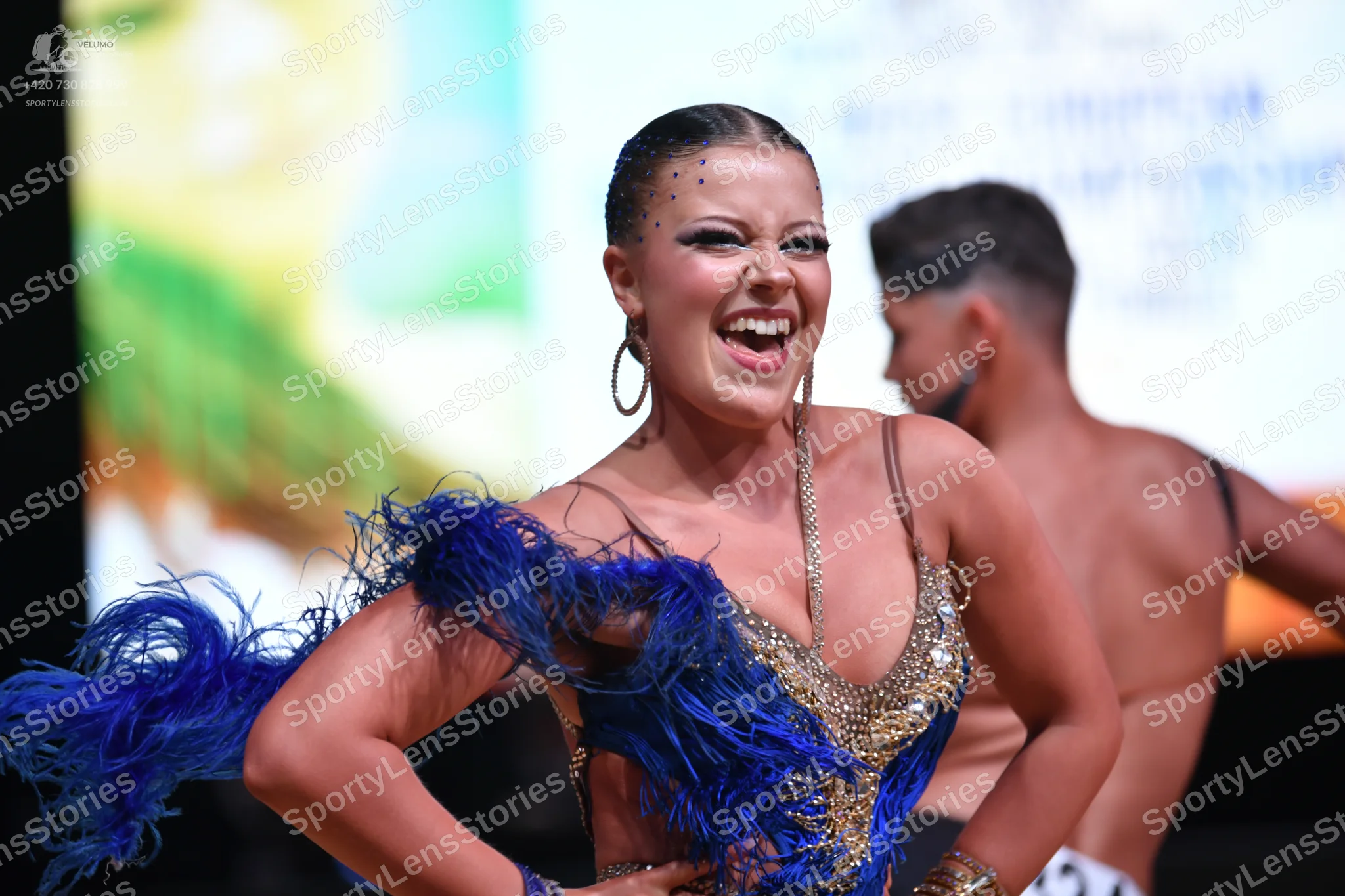 Dancesport competitor: Female dancer: blue and gold sequined latin dress with large blue feather accent