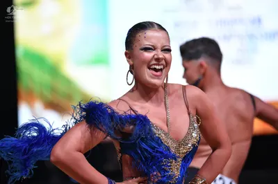 Dancesport competitor: Female dancer: blue and gold sequined latin dress with large blue feather accent