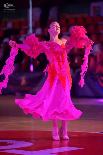 Dancesport competitor: Female dancer: bright pink ballgown with large, voluminous ruffled sleeves and a