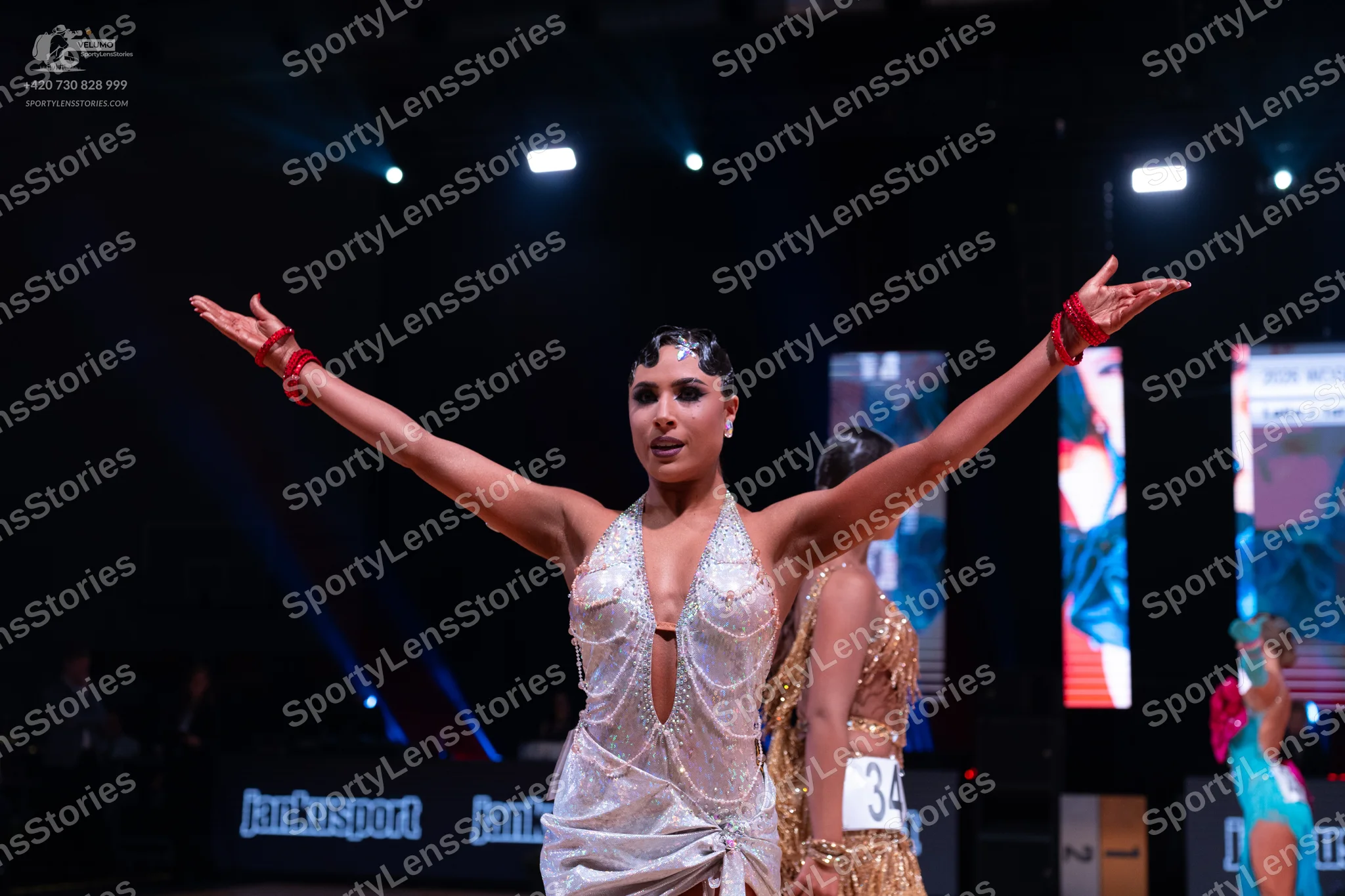 Dancesport competitor: Main female dancer: white/silver latin dress with a deep V-neckline, featuring b