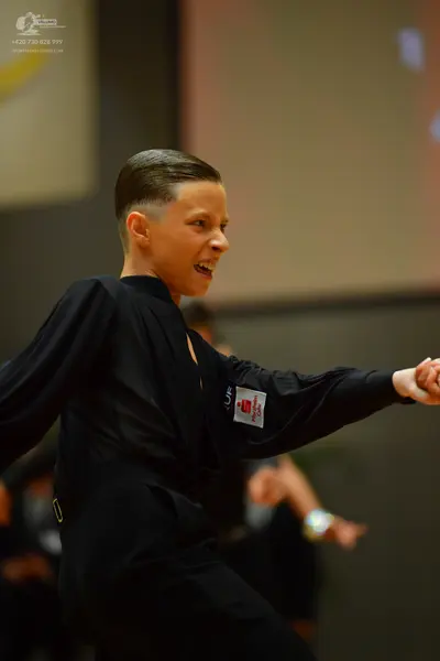 Dancesport competitor: Male dancer: black long-sleeved shirt and trousers with a small red and white pa