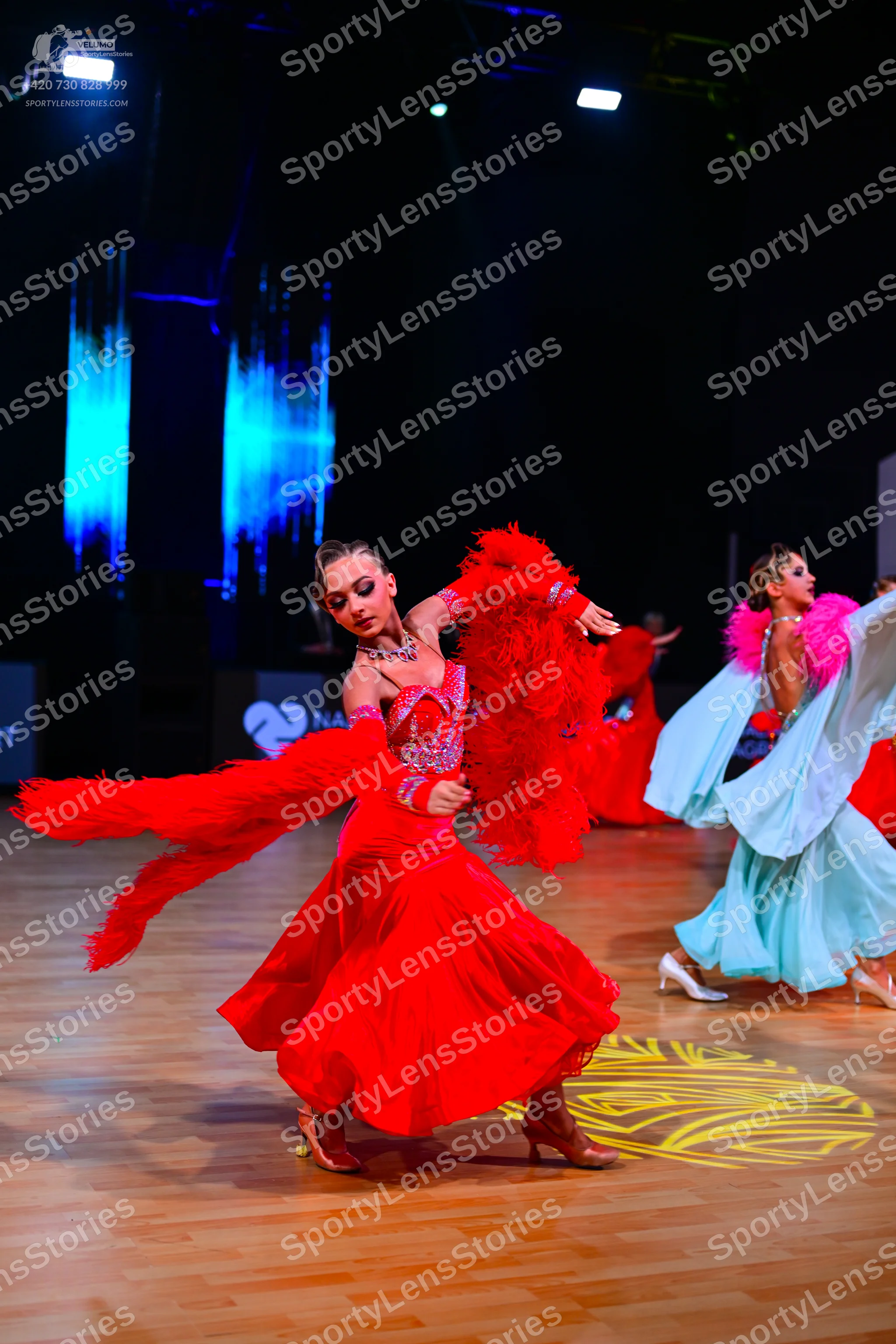 Dancesport competitor: Female dancer 1: red latin dress with voluminous red feather-like trim on the sl