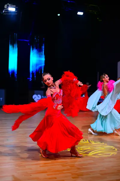 Dancesport competitor: Female dancer 1: red latin dress with voluminous red feather-like trim on the sl