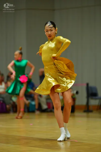 Dancesport competitor: Female dancer in foreground: gold metallic long-sleeved Latin dress