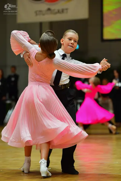 Dancesport competitor: Female dancer in foreground: light pink long-sleeved dress with a pleated skirt