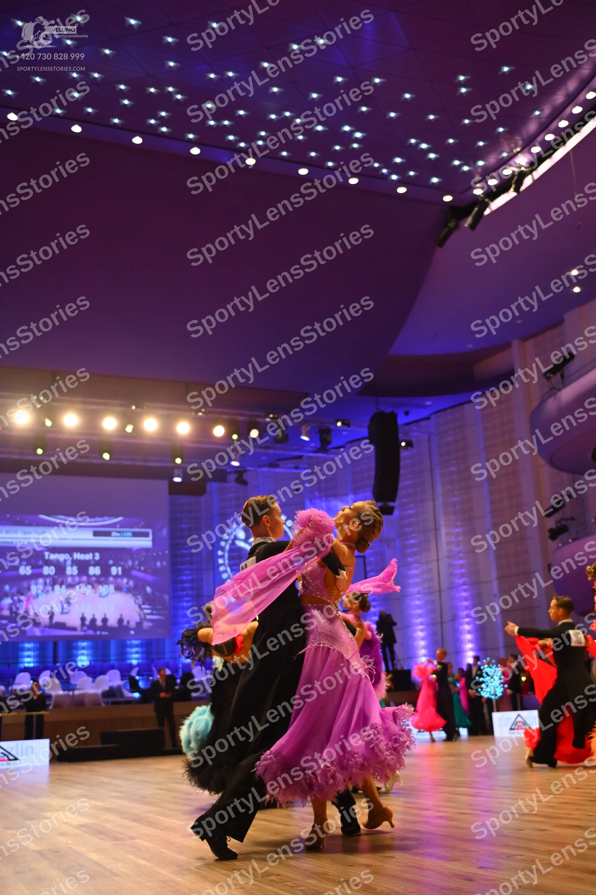 Dancesport competitor: Foreground female dancer: pink latin dress with a layered, frilled skirt