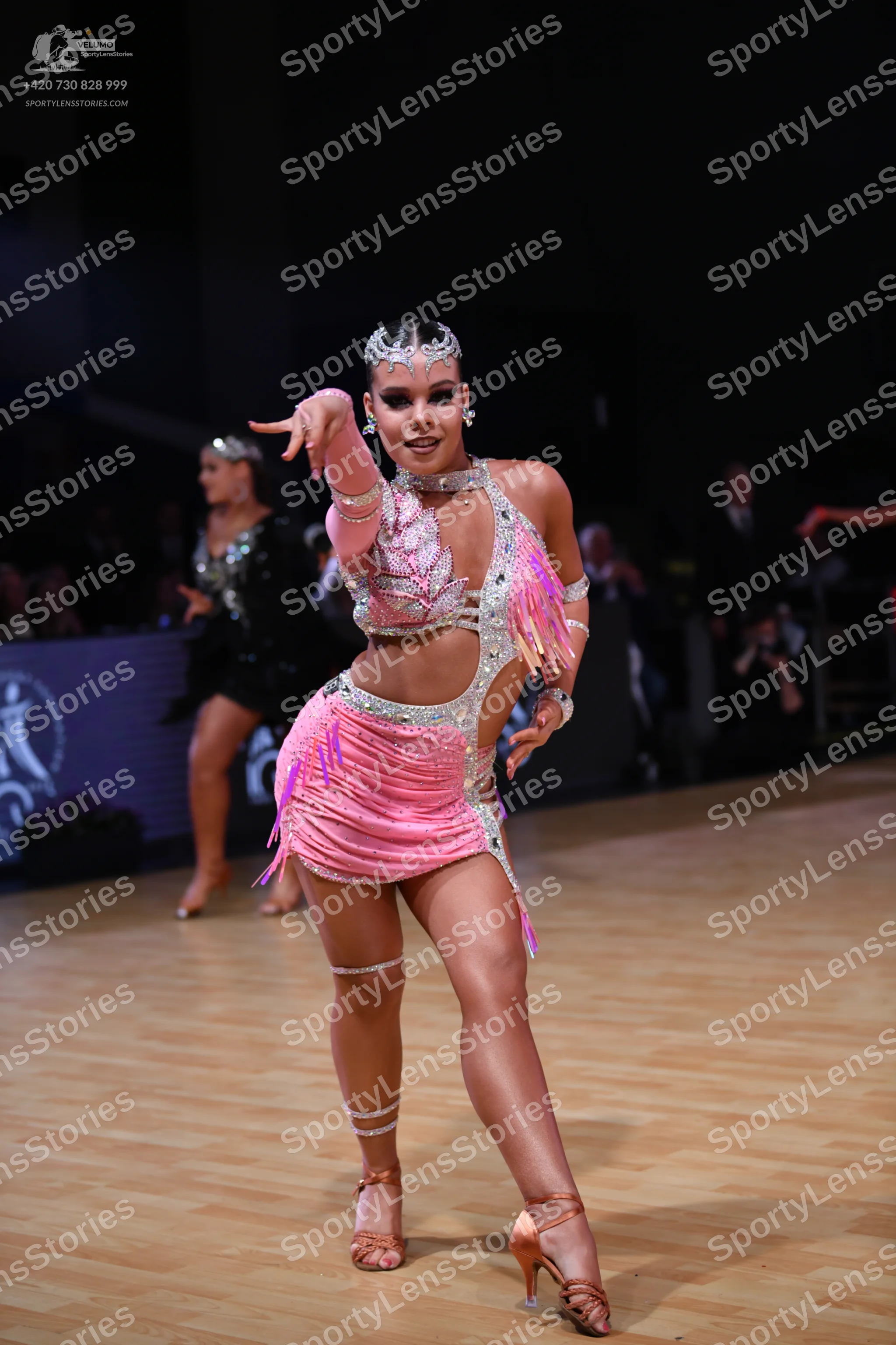 Dancesport competitor: Female dancer (foreground): pink latin costume with sequins, fringe, and nude me