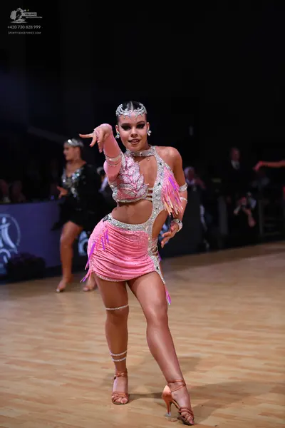 Dancesport competitor: Female dancer (foreground): pink latin costume with sequins, fringe, and nude me