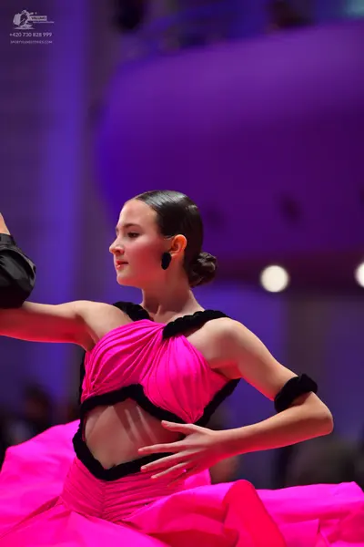 Dancesport competitor: Female dancer: bright pink ballgown with a pleated bodice, black trim around the