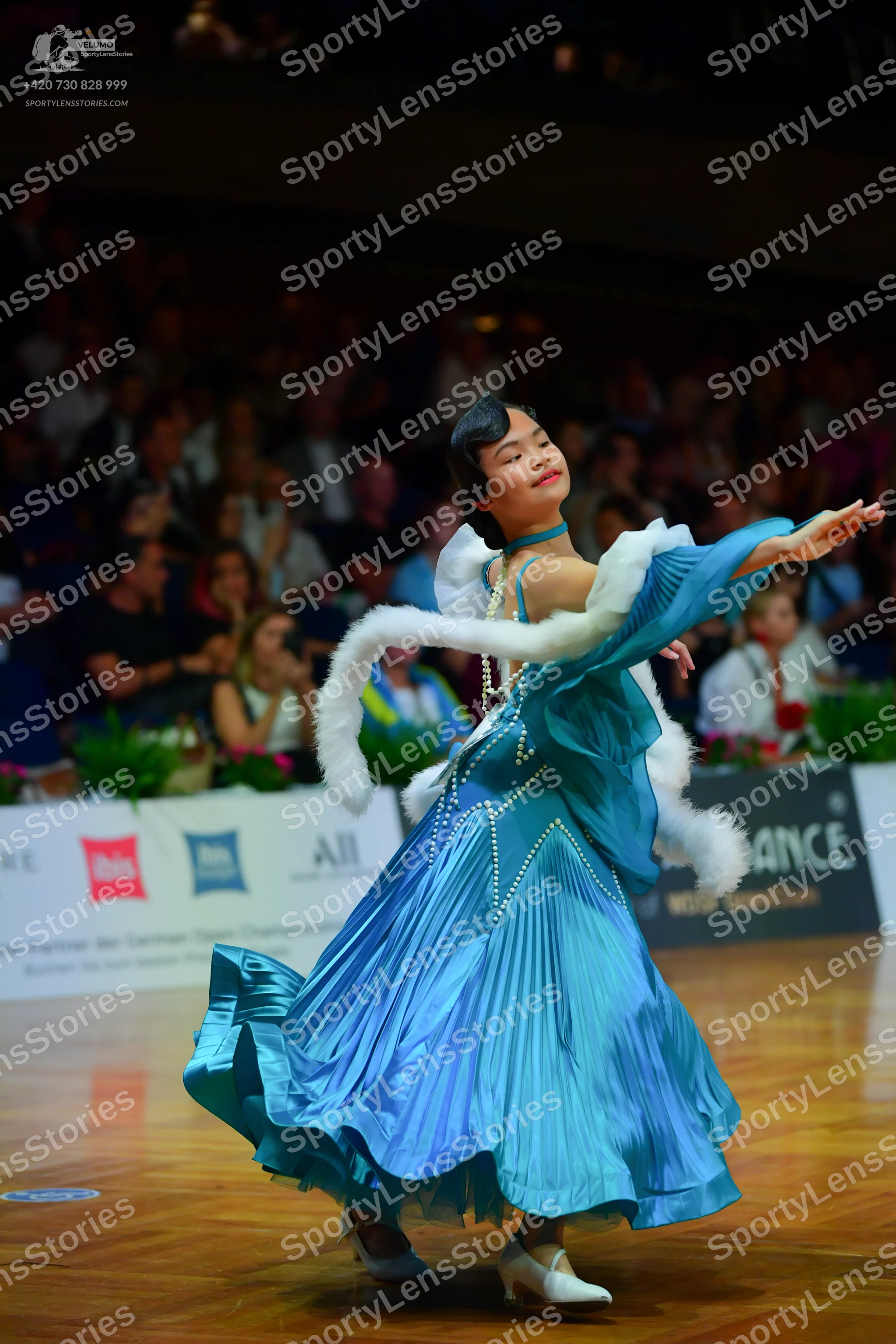 Dancesport competitor: Female dancer: teal ballroom gown made of a shiny, satin-like fabric with vertic