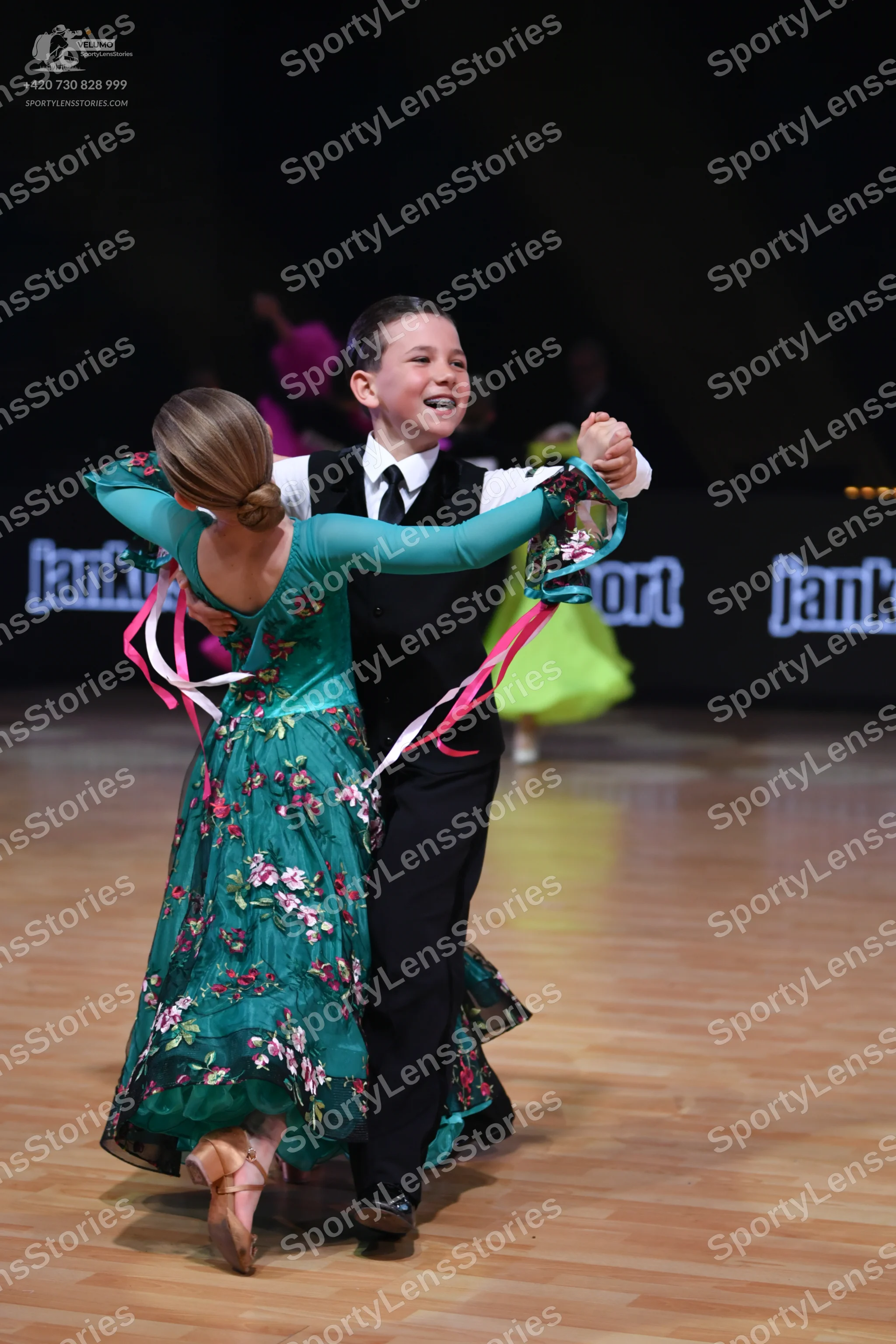 Dancesport competitor: Female dancer: teal ballgown with long sleeves and pink/white floral pattern, wi