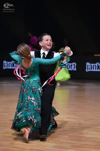 Dancesport competitor: Female dancer: teal ballgown with long sleeves and pink/white floral pattern, wi