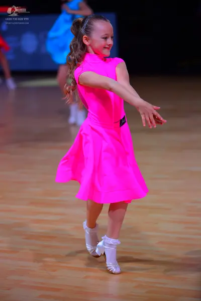 Dancesport competitor: Female dancer in foreground: bright pink, short, flared, sleeveless dress in a s
