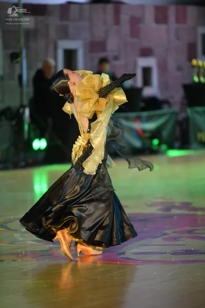 Dancesport competitor: Female dancer: black satin ballroom gown with large, voluminous gold-colored ruf