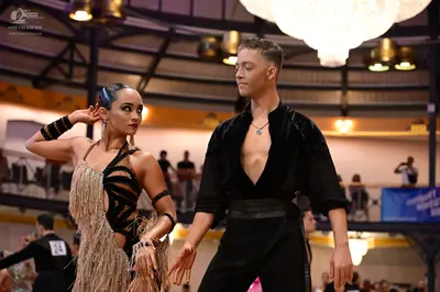 Dancesport competitor #24: Female dancer: gold and black latin dance dress with fringe and black wristbands
