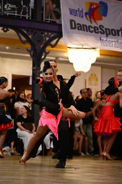 Dancesport competitor: Female dancer in center: black long-sleeved top and pink fringe skirt