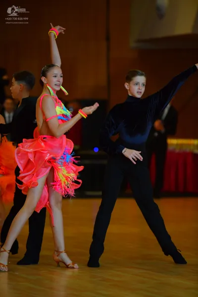 Dancesport competitor: Female dancer: bright pink latin dress with yellow and blue fringe and spaghetti