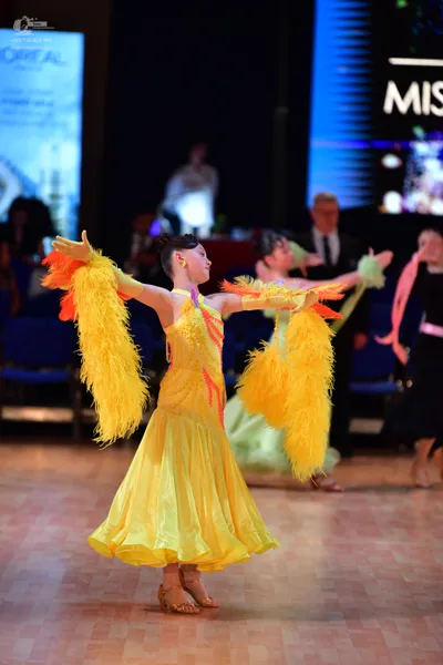 Dancesport competitor: Female dancer: yellow latin dress with large yellow feather boas on the arms