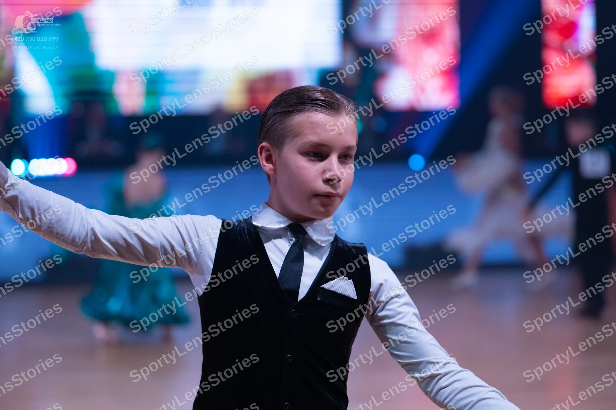 Dancesport competitor: Male dancer in foreground: white long-sleeved shirt, black necktie, and black wa