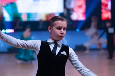 Dancesport competitor: Male dancer in foreground: white long-sleeved shirt, black necktie, and black wa