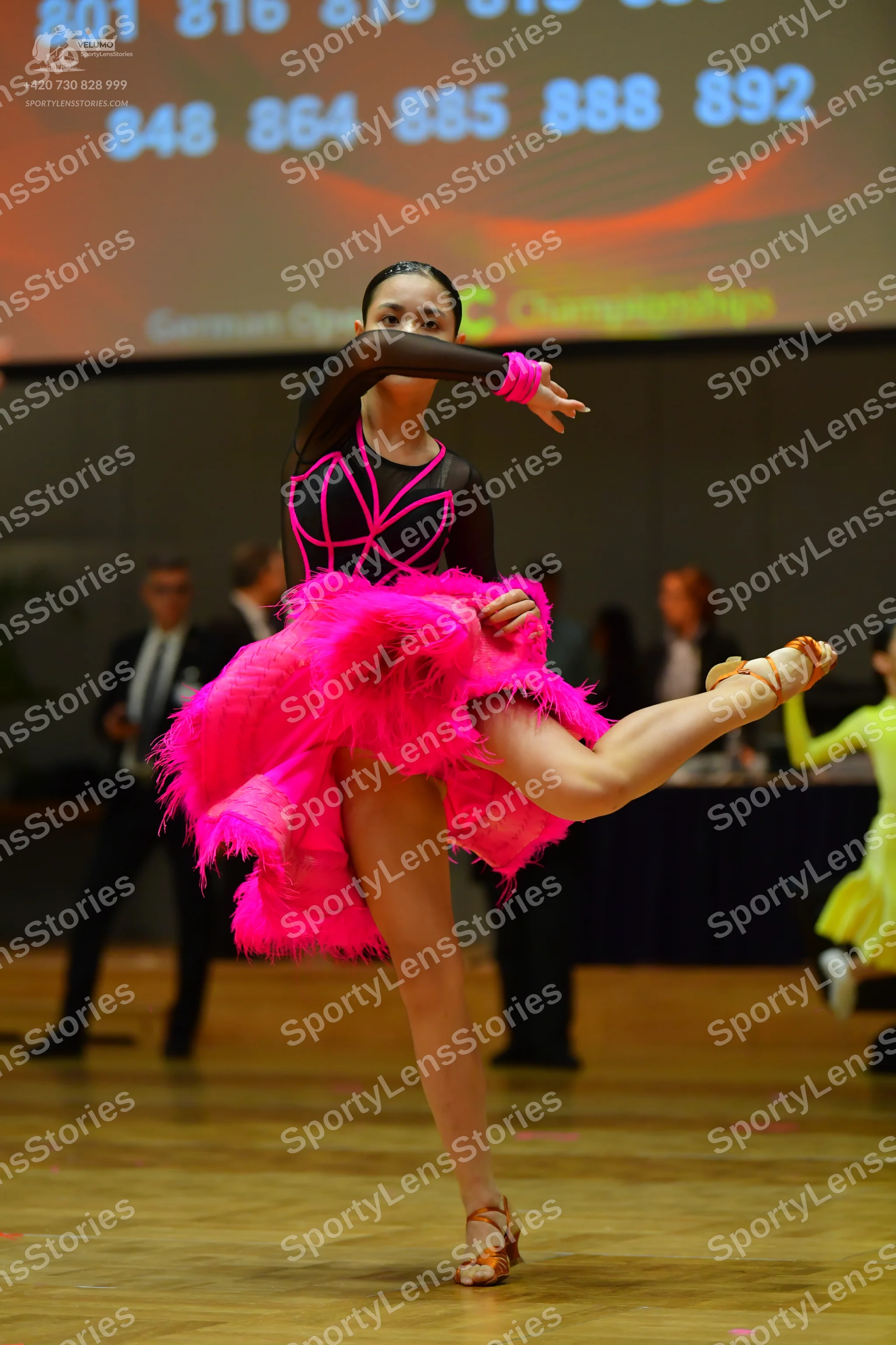 Dancesport competitor: Female dancer in foreground: black long-sleeved latin dance top with pink accent
