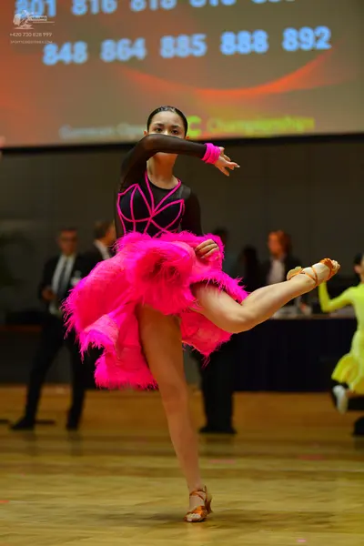 Dancesport competitor: Female dancer in foreground: black long-sleeved latin dance top with pink accent